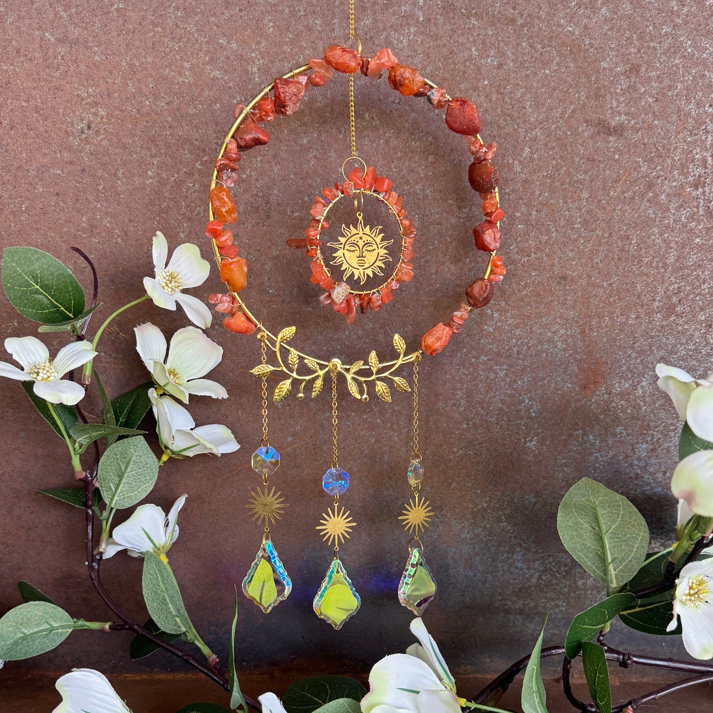 Decorative Crystal Sun Catcher - Red Jasper hanging ornament with stones and sun design, surrounded by flowers and leaves on a brown background.