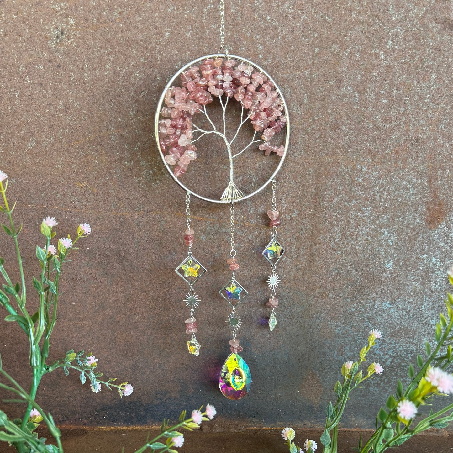 Decorative Decorative Tree of Life Crystal Sun Catcher - Strawberry Quartz hanging ornament with tree design and colorful beads against a textured brown background