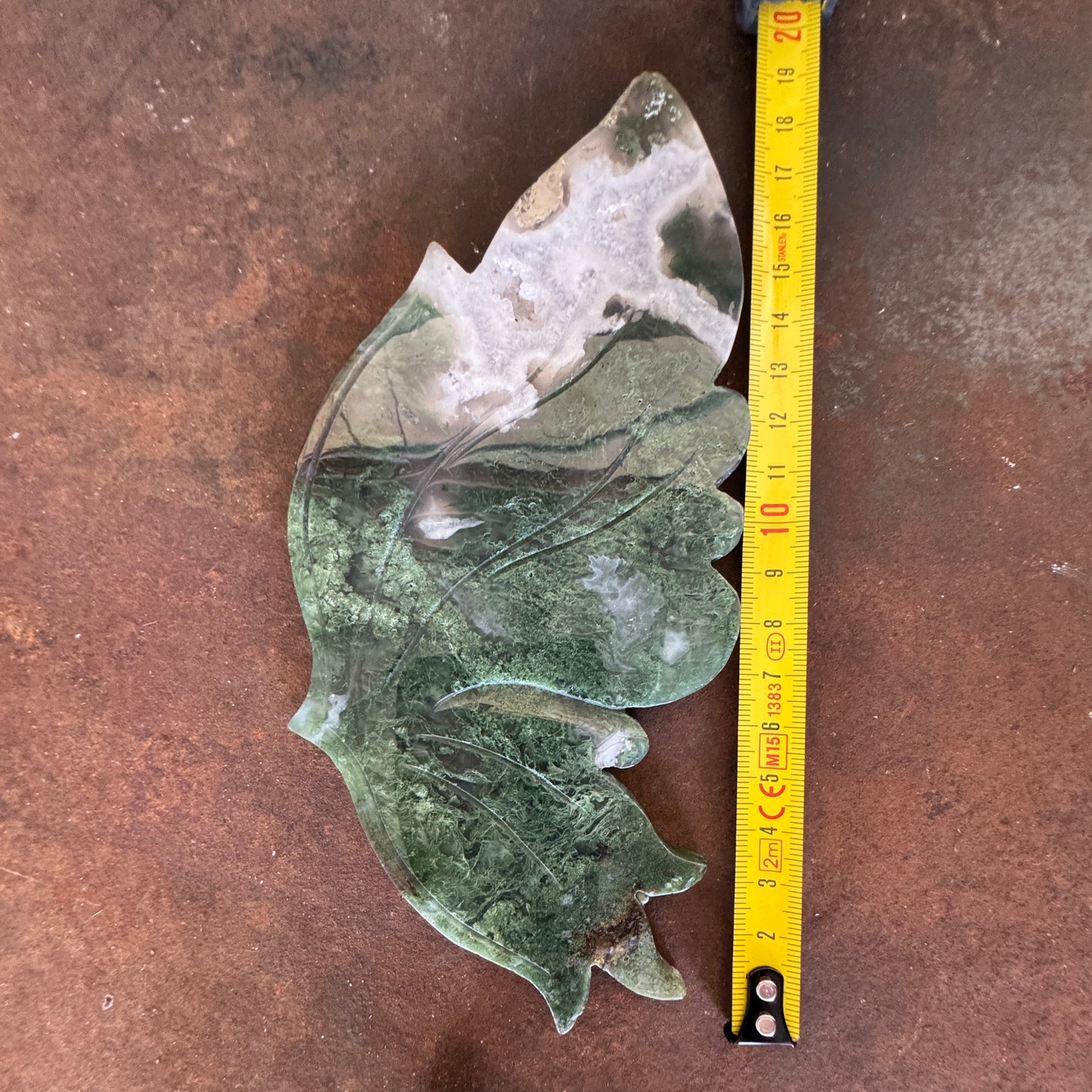 Moss Agate Crystal Wing beside measuring tape on a brown surface