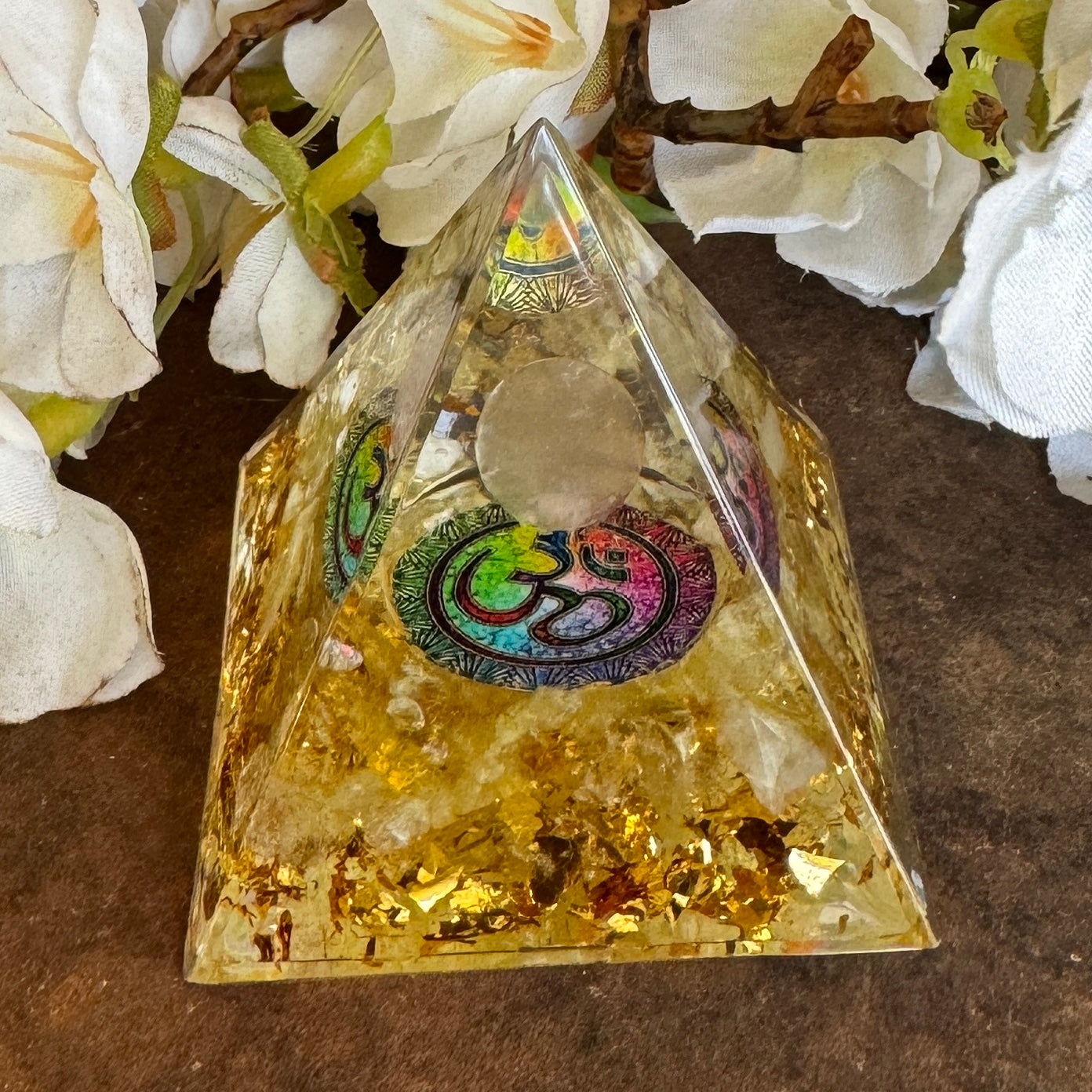 A clear Orgonite pyramid with gold accents and a combination of Citrine, a Clear Quartz Sphere, and an Om Symbol on the top.