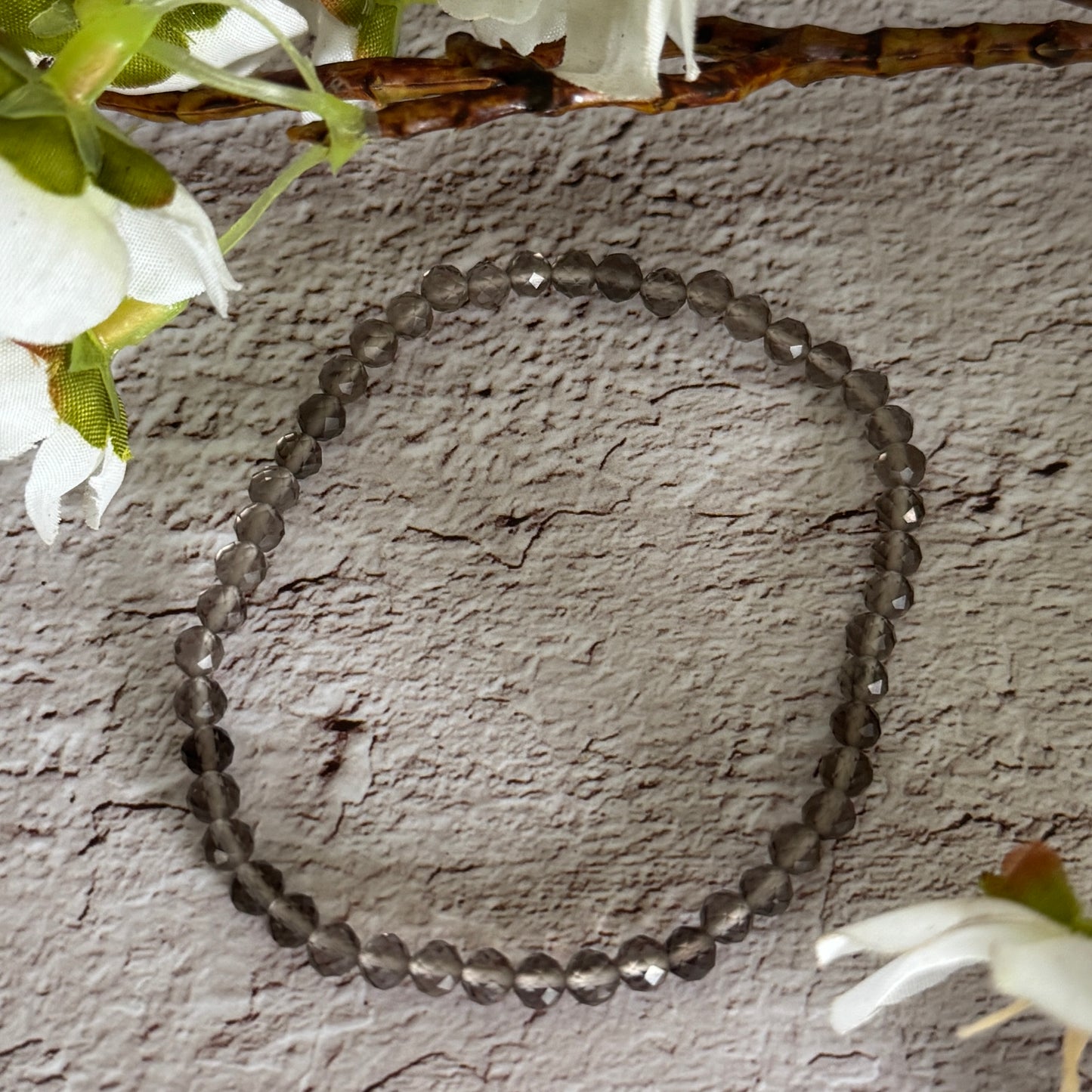 A bracelet featuring faceted smoky quartz beads on a textured background with flowers.