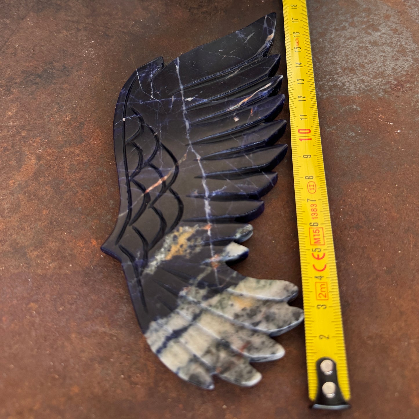 Decorative stone wing with a measuring tape for scale on a brown surface