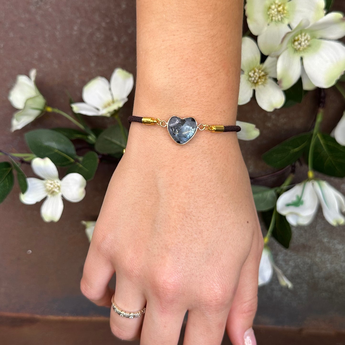 Hand wearing a bracelet with a heart-shaped charm against a floral background