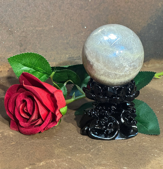 A black resin lotus flower sphere holder with a spherical crystal displayed on top, accompanied by a red rose and green leaves in the background.