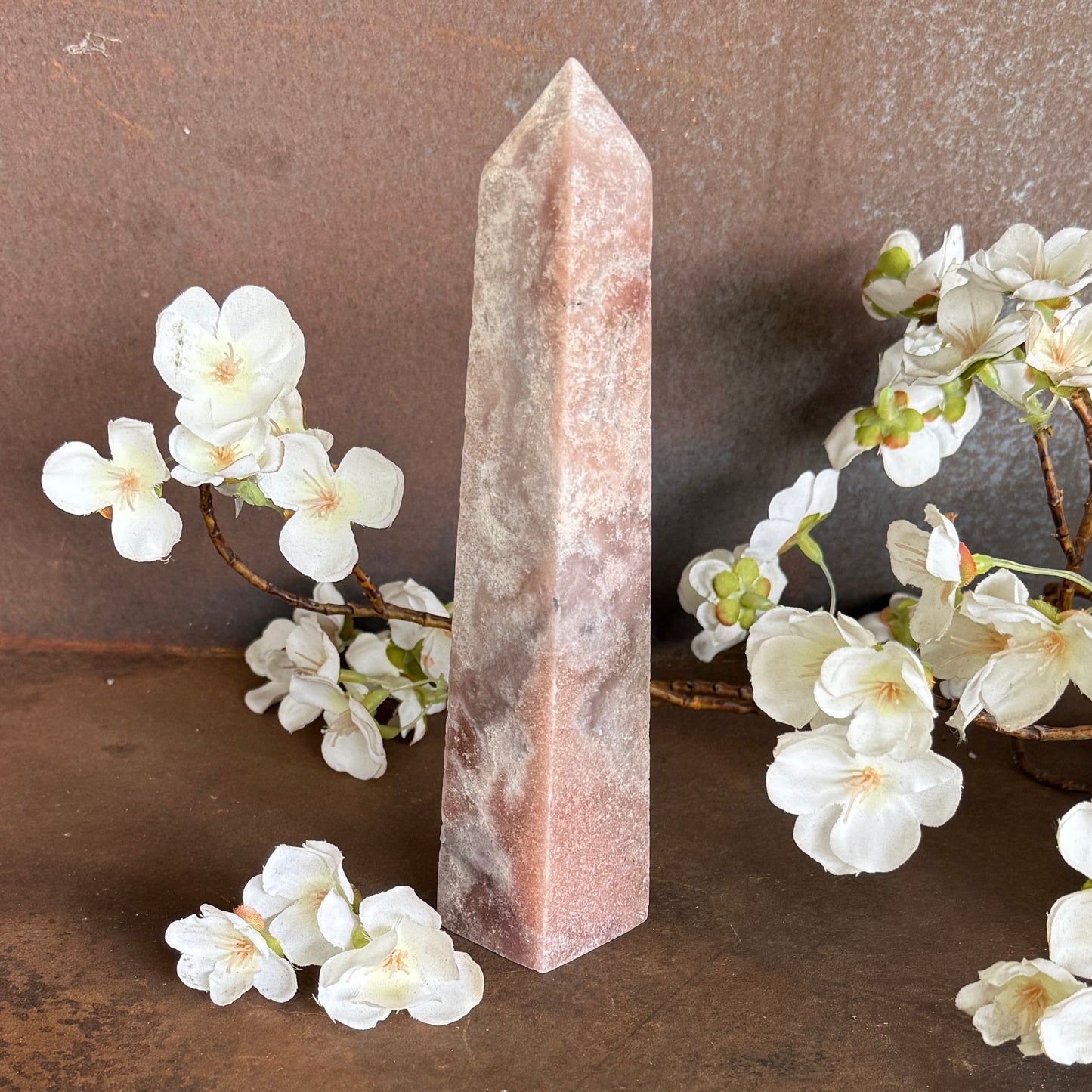 Pink Amethyst obelisk with white flowers on a brown surface
