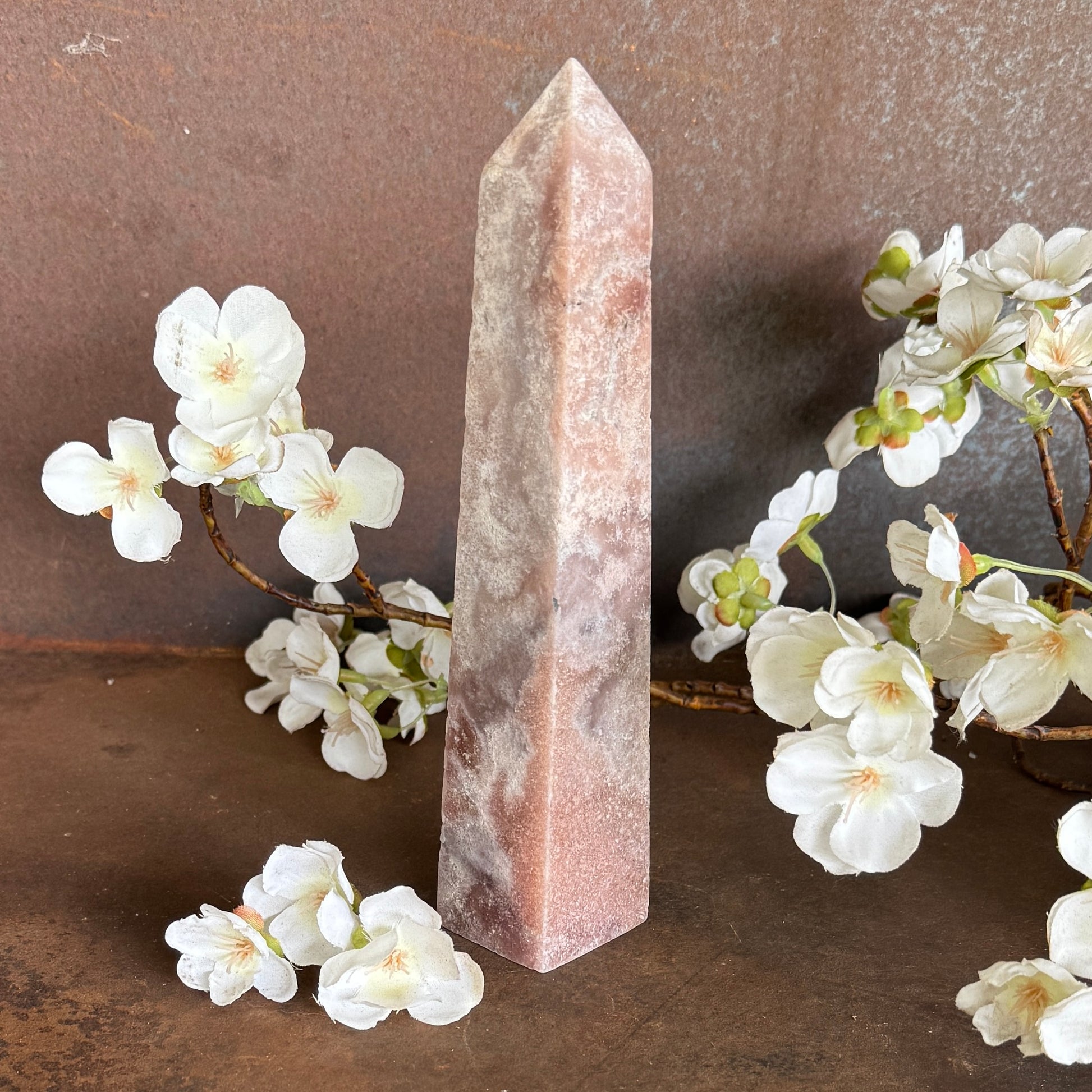 Pink Amethyst obelisk with white flowers on a brown surface
