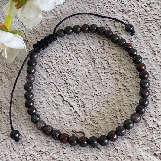 An adjustable Poppy Jasper bracelet with 4mm beads displayed on a textured surface with white flowers in the background.