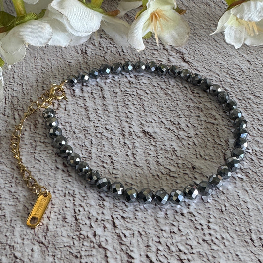 A bracelet made of faceted Terahertz beads with an adjustable gold chain, displayed on a textured background with white flowers.