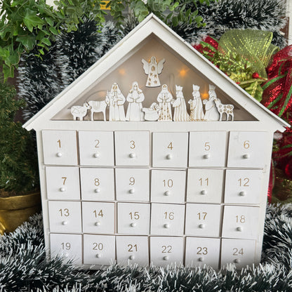 White house-shaped Advent calendar with Nativity scene figures on a Christmas-themed background.
